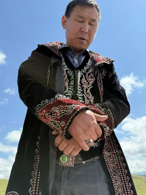 努开,身着哈萨克传统刺绣袷袢立于草原